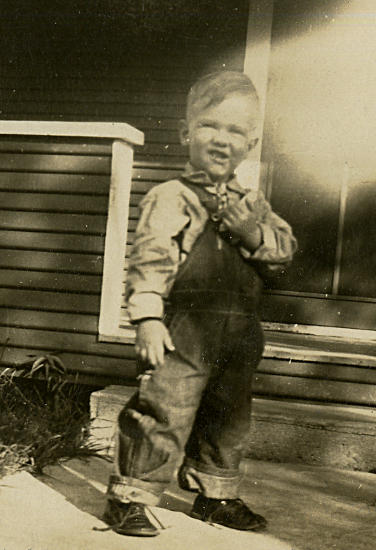 photograph of a young J. W. Fiegenbaum wearing overalls and posing for his portrait in front of the home in Miami, Oklahoma