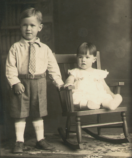 photographic portrait of a very young J. W. standing beside his sister, Dorothy L. Fiegenbaum, seated in a rocking chair